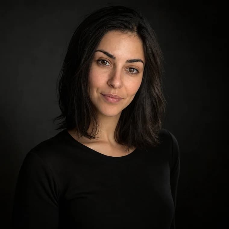 An editorial headshot with dramatic side lighting against a near-black backdrop